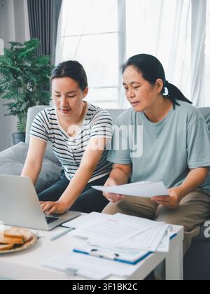 Asian mother and adult daughter using laptop with documents at home, concept of family finance, insurance planning, online banking, paperwork, and car Stock Photo