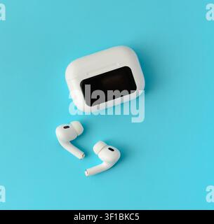White wireless earbuds with a closed charging case on a blue background. Minimal technology composition for music, communication and everyday use Stock Photo
