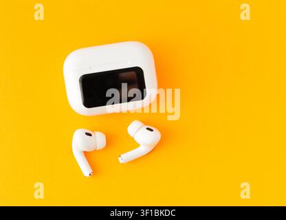 White wireless earbuds with a charging case on a yellow background. Minimal technology concept for music, communication and modern mobile lifestyle Stock Photo