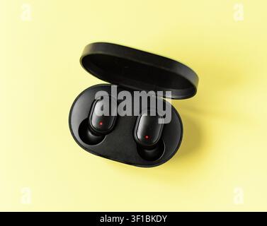 Black wireless earbuds in an open charging case on a yellow background. Minimal technology concept for music, communication, remote work and everyday Stock Photo