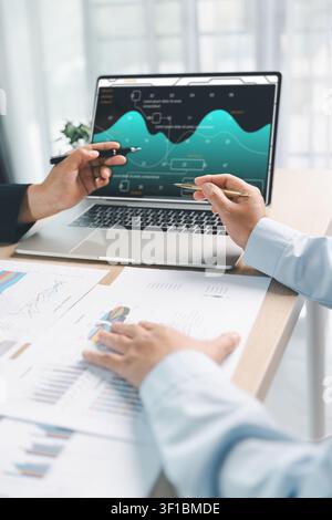 Business colleagues presenting financial dashboard on laptop during office meeting, showing data analytics, sales performance, strategy planning and t Stock Photo