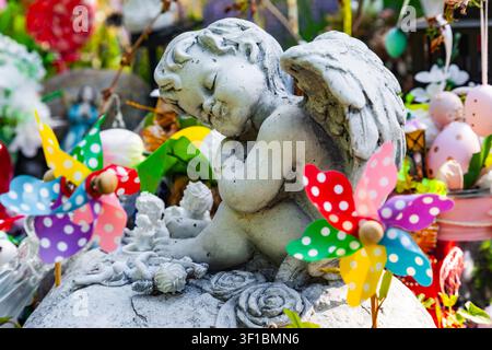 Small stone angel statue with wings surrounded by colorful polka dot pinwheels and easter eggs decorations in a garden Stock Photo