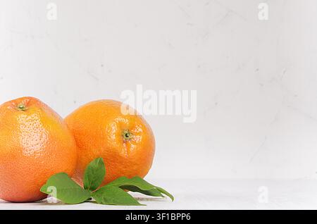 Two fresh glossy whole grapefruits with green leaves closeup on white wooden background with copy space. Stock Photo