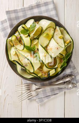 Zucchini carpaccio with pistachios, chili pepper and mint close-up in a plate on the table. Vertical top view from above Stock Photo