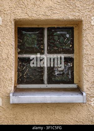 Germany 2026 Textured plaster wall holds square window niche with four dark glass panes, worn white frame, and shallow stone ledge, creating rustic ar Stock Photo