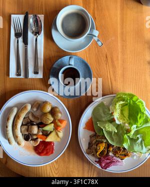 Overhead flat lay of a healthy breakfast spread featuring coffee, sausages, fresh salad, vegetables and potatoes served on a wooden table in a modern Stock Photo