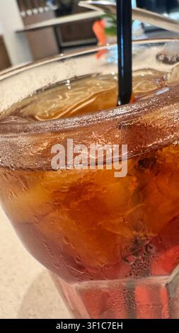 Close-up of iced tea served in a clear glass with ice cubes and a drinking straw on a café table, capturing a refreshing non-alcoholic beverage. Stock Photo