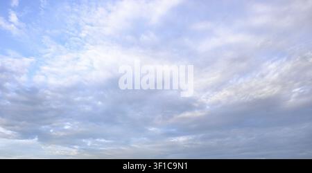 A vast expanse of gentle white and grey wispy clouds drifting calmly across a bright blue afternoon sky backdrop. Stock Photo