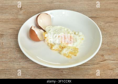 fried egg with creamy yolk pouring from shell arranging on plate Stock Photo