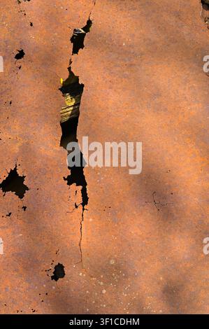 Rusty iron sheet shows distressed vintage background. Corroded metallic surface features huge vertical crack and dark hole. Old metal plate brings ind Stock Photo