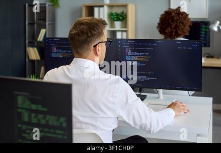 Programmer coding at dual monitors in collaborative modern software office Stock Photo