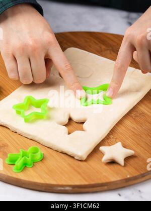 Child's hands cutting shapes with green cookie cutters from rolled dough on wooden board for baking cookies close-up Stock Photo
