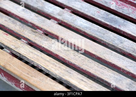 Wooden slats forming a bench surface show a weathered texture with peeling red paint, revealing the natural wood grain and creating an aged, rustic ba Stock Photo