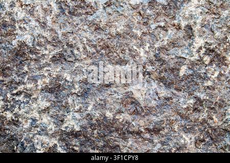 Detailed view of a natural granite stone showing its coarse grain, crystalline structure, and speckled coloration with shades of grey, brown, and whit Stock Photo