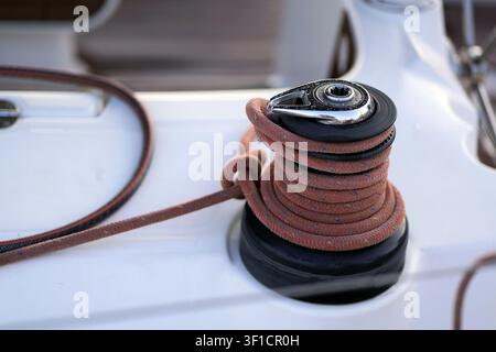 Sailboat winch with orange rope carefully coiled on its drum, ready for managing boat rigging, showcasing marine equipment up close on a yacht deck Stock Photo