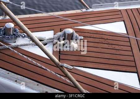 Sailboat deck featuring a stainless steel cleat with mooring rope tied securely, highlighting maritime equipment and teak decking Stock Photo