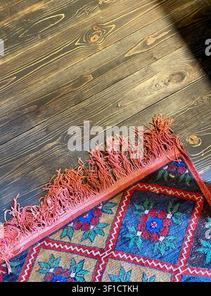 Traditional woven rug on dark wooden floor with rustic texture and ethnic pattern. Stock Photo