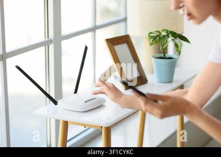 Person using a smartphone near a white wifi router on a table, home internet connection and modern technology Stock Photo