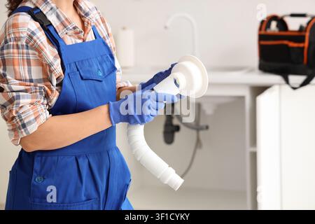 Plumber in blue overalls and gloves holding a sink drain pipe, home repair and maintenance service, the worker is focused on the plumbing component Stock Photo