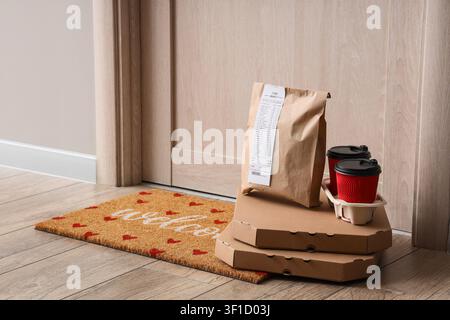 Contactless food delivery service with pizza boxes, paper bag, and coffee cups left at a residential doorstep Stock Photo