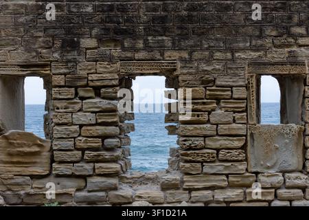 Weathered ancient stone wall with rectangular openings overlooking the sea. Stock Photo