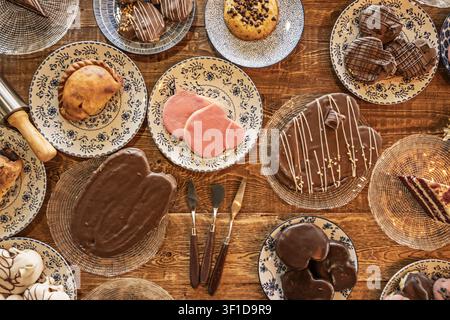 Overhead view of assorted baked goods including chocolate-covered heart cakes, pink frosted cookies, a golden empanada, and chocolate chip cookies arr Stock Photo