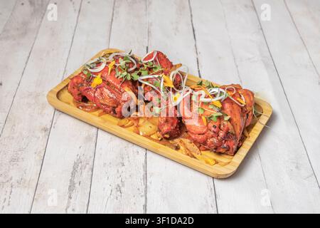 Juicy red marinated chicken pieces served on a rectangular bamboo platter with caramelized onions, garnished with fresh microgreens, white onion rings Stock Photo