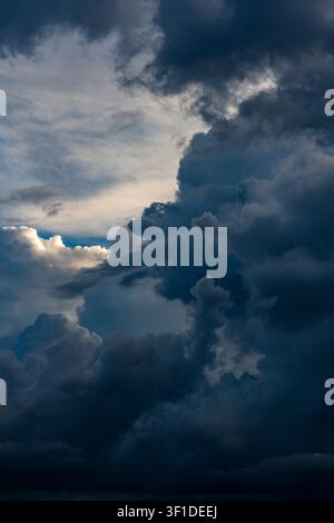 Dramatic dark storm clouds in deep blue sky. Vertical view of heavy dark storm clouds accumulating in blue sky, creating dramatic and powerful weather Stock Photo