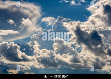 Dynamic blue sky filled with dramatic cumulus clouds. Beautiful sky background with fluffy white and dark cumulus clouds contrasting against a bright Stock Photo