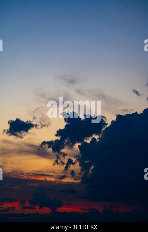 Dramatic sunset sky with dark silhouettes of clouds. Beautiful sunset sky with dark cloud over vibrant orange red and deep blue gradients representing Stock Photo