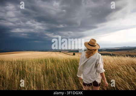 Worried female farmer looking at approaching storm clouds over agricultural field. Summer weather and impact climate change on agriculture concept Stock Photo