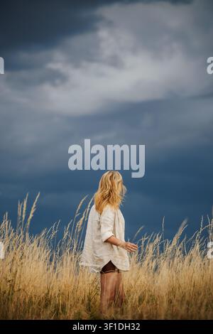 Woman standing in dry grass and looking at approaching storm clouds on horizon. Summer weather Stock Photo