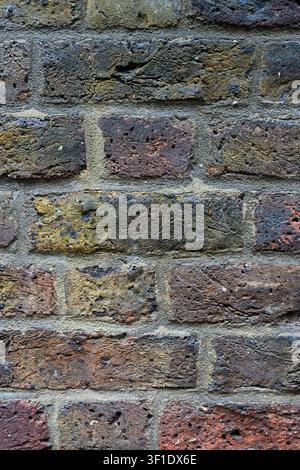 Aged and weathered multi colored rough texture brick wall background with dirt and grim Stock Photo
