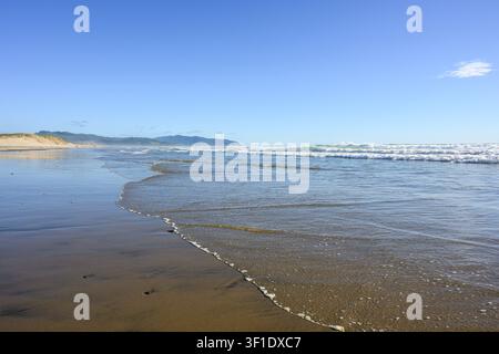 Background of gentle wave rolling onto sandy beach with blue sky and ocean waves Stock Photo