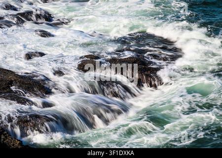 Ocean waves drain over coastal rocks on shoreline in silky motion Stock Photo