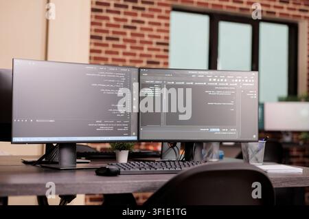Empty IT office desk shows computer monitors running terminal windows, artificial intelligence database scripts and server cloud computing code in a software workspace. Stock Photo