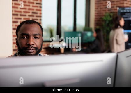 African American programmer develops a scalable security application in a software office, working with advanced technology and layered digital systems. Stock Photo