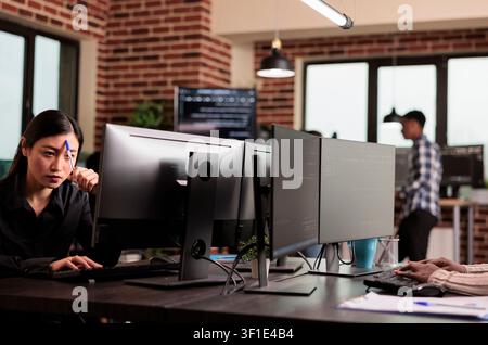 Pensive engineer develops HTML script while developing cloud computing data, HTML scripts and algorithms on a workplace computer inside an IT office. Stock Photo