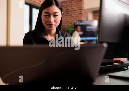 Asian tech engineer analyzing compiling html code on computer display, working on interface development, software developer using terminal window with firewall server data in it big data agency. Stock Photo