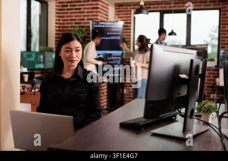 Asian programmer typing machine learning server code, sitting at desk table in it software company, programming engineer working on database system with coding script in it developing office. Stock Photo