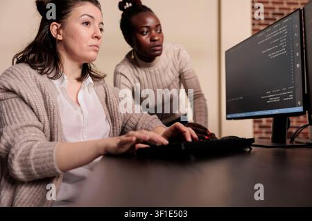 Diverse engineering team discusses programming in an IT development agency while a developer compiles app language and server algorithms. Stock Photo