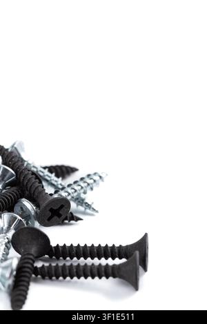 Black and silver screws lie scattered on white. Some have sharp points, others flat heads. Metallic sheen contrasts with matte black finish. Close-up Stock Photo