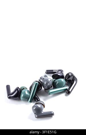 Black and green earbuds scattered on a clean white surface. Minimalist composition highlights modern tech design. Sleek shapes contrast with smooth, g Stock Photo