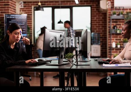 Pensive Asian programmer brainstorms ideas while developing HTML script and thinking about database server logic inside an IT agency office. Stock Photo