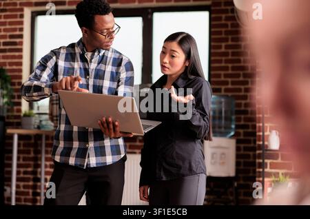 Diverse coders looking at security firewall on laptop, using html and terminal window, working in it programming office, software developers to program software using cloud computing app server. Stock Photo