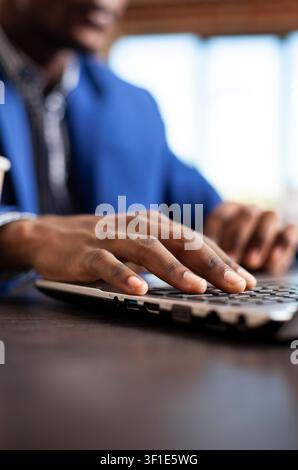 Hands of african american employee typing on laptop at startup office desk, Black male individual updating company research data using digital technology for work tasks. Stock Photo