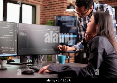 Programmers reviewing HTML code together in startup office while working with code, screens and digital infrastructure for software development. Stock Photo