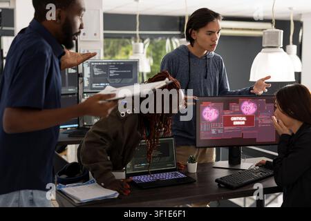 Diverse team of software developers works anxiously to resolve unexpected system crash in modern office. Worried Asian woman collaborates with colleagues on troubleshooting critical technical error. Stock Photo
