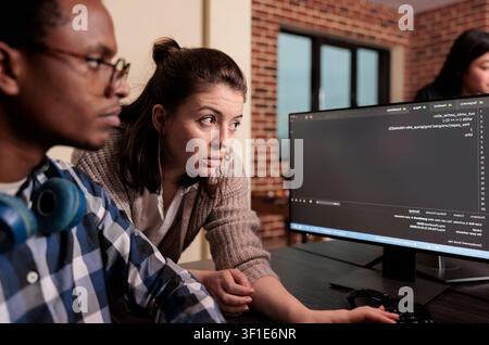 Tech engineer asking app designer for help with html code, pointing at database script on terminal window, Team of programming engineers working on app developing program in it agency. Stock Photo