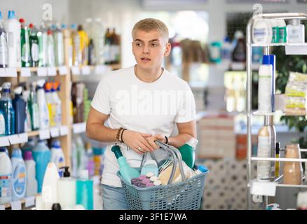 Guy selects various household cleaning products for cleaning the house with full basket of various purchases Stock Photo